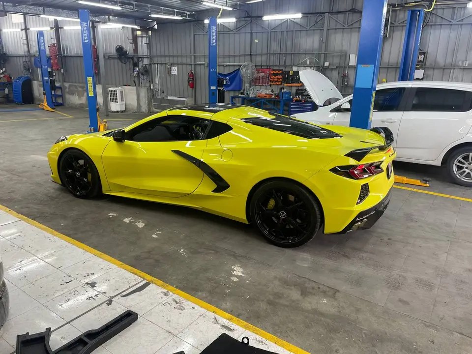 Chevrolet Corvette 2022: На фото — желтый Chevrolet Corvette 2022, стоящий в гараже. Видны черные колеса, боковые воздухозаборники и задние фонари. На полу лежат снятые детали кузова.
