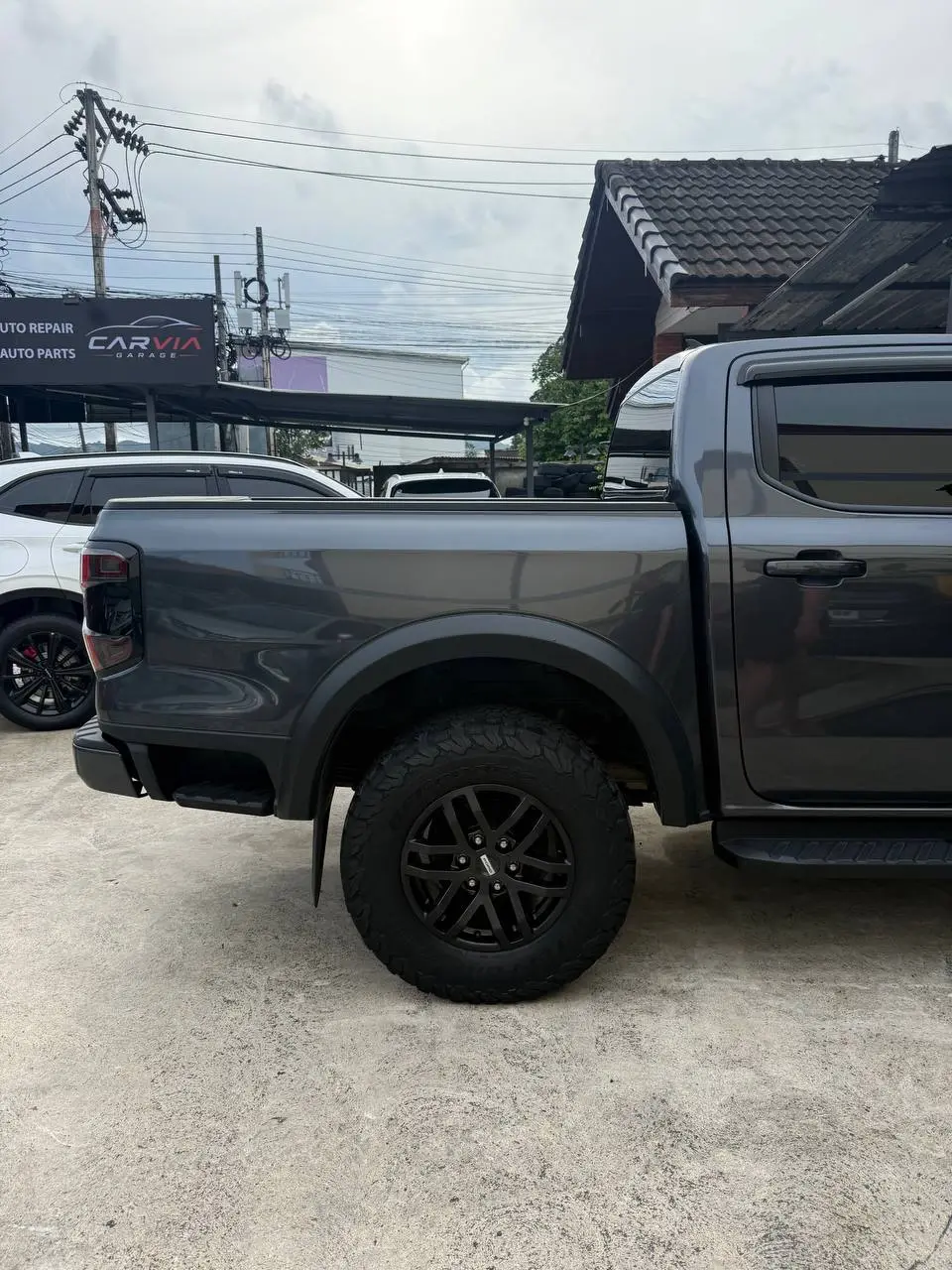 Ford Ranger 2025: На фото видна задняя часть серого пикапа Ford Ranger 2025 с черными колесами и бортами. Автомобиль стоит на улице у автосервиса Carvia Garage.