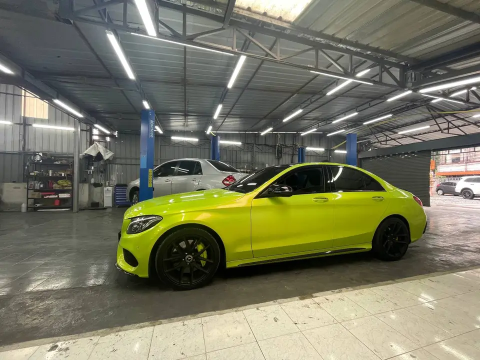 Mercedes-Benz C350e 2018: На фото — ярко-жёлтый седан Mercedes-Benz C350e 2018, стоящий в гараже. Автомобиль оснащён чёрными колёсными дисками и выглядит как готовый к сдаче после обслуживания. Видны 